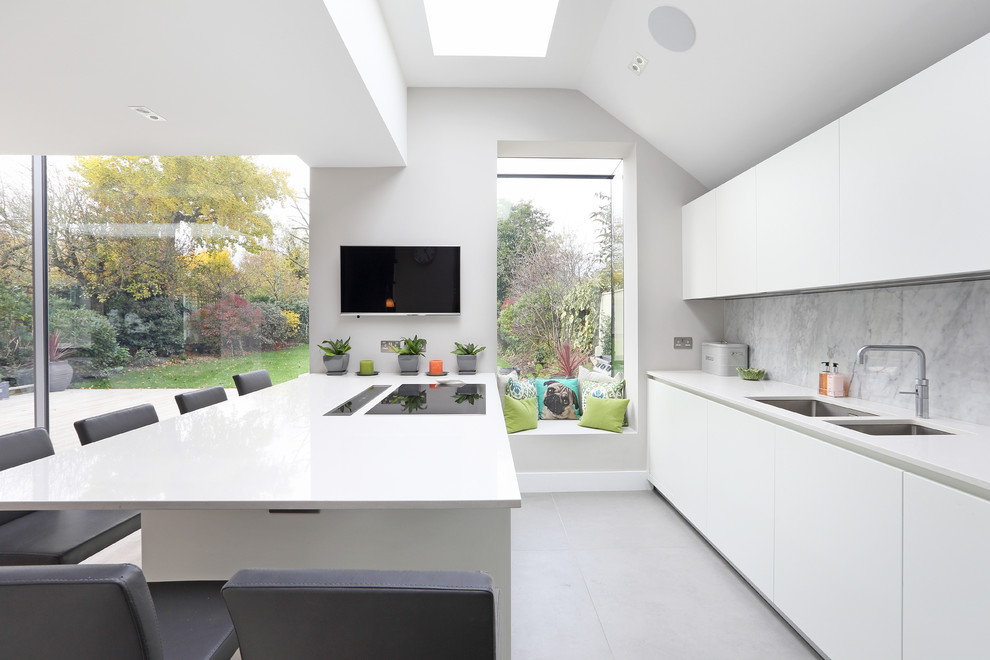 Пример оригинального дизайна: кухня в современном стиле с двойной мойкой, плоскими фасадами, белыми фасадами, серым фартуком, полуостровом, серым полом, белой столешницей и телевизором