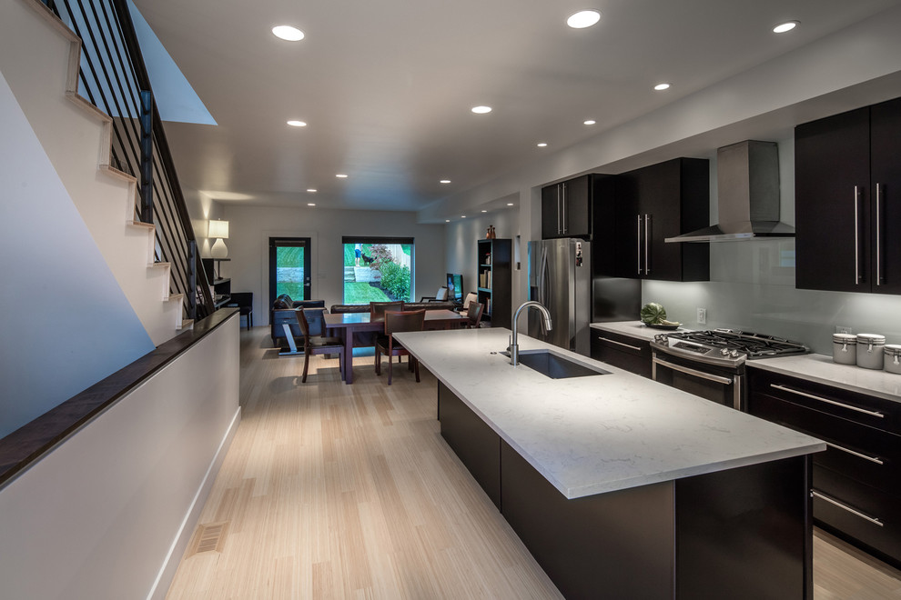 Photo of a medium sized modern galley kitchen/diner in St Louis with a single-bowl sink, flat-panel cabinets, dark wood cabinets, engineered stone countertops, white splashback, glass sheet splashback, stainless steel appliances, bamboo flooring and an island.