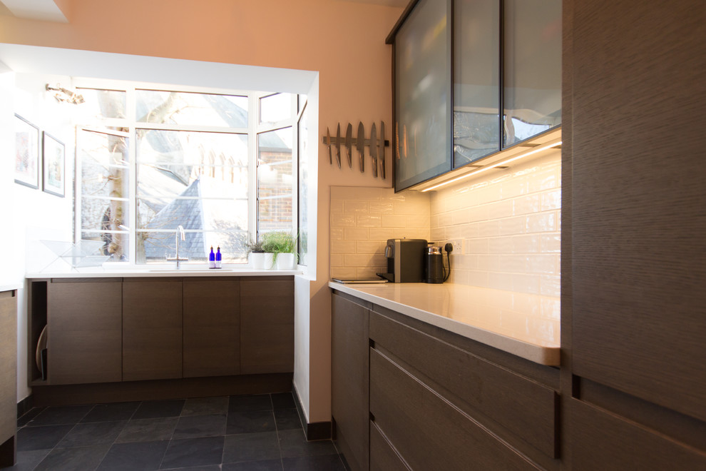 Design ideas for a small contemporary u-shaped enclosed kitchen in London with an integrated sink, glass-front cabinets, brown cabinets, quartz worktops, white splashback, ceramic splashback, stainless steel appliances, slate flooring and no island.
