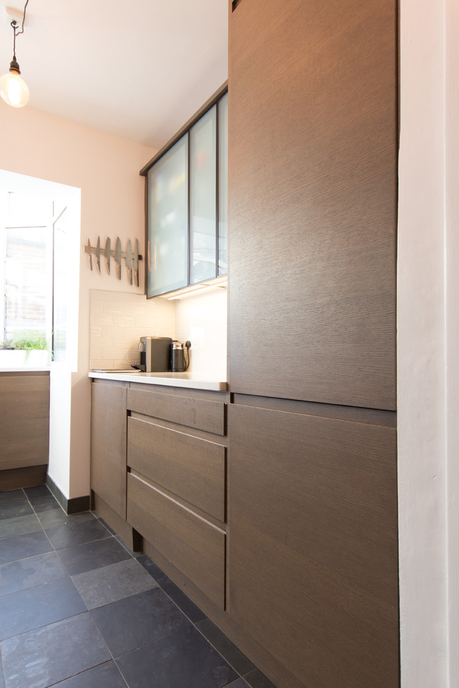 This is an example of a small contemporary u-shaped enclosed kitchen in London with an integrated sink, glass-front cabinets, brown cabinets, quartz worktops, white splashback, ceramic splashback, stainless steel appliances, slate flooring and no island.