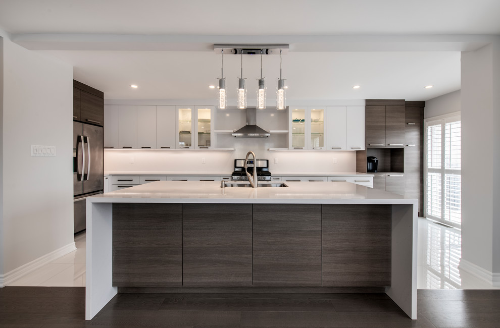 Large contemporary l-shaped open plan kitchen in Toronto with a submerged sink, flat-panel cabinets, white cabinets, quartz worktops, white splashback, stone slab splashback, stainless steel appliances, porcelain flooring, an island, white floors and white worktops.