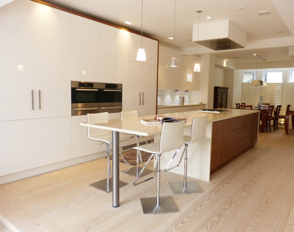 Exempel på ett modernt kök, med en undermonterad diskho, släta luckor, vita skåp, bänkskiva i kvarts, vitt stänkskydd, glaspanel som stänkskydd, rostfria vitvaror, ljust trägolv och en köksö