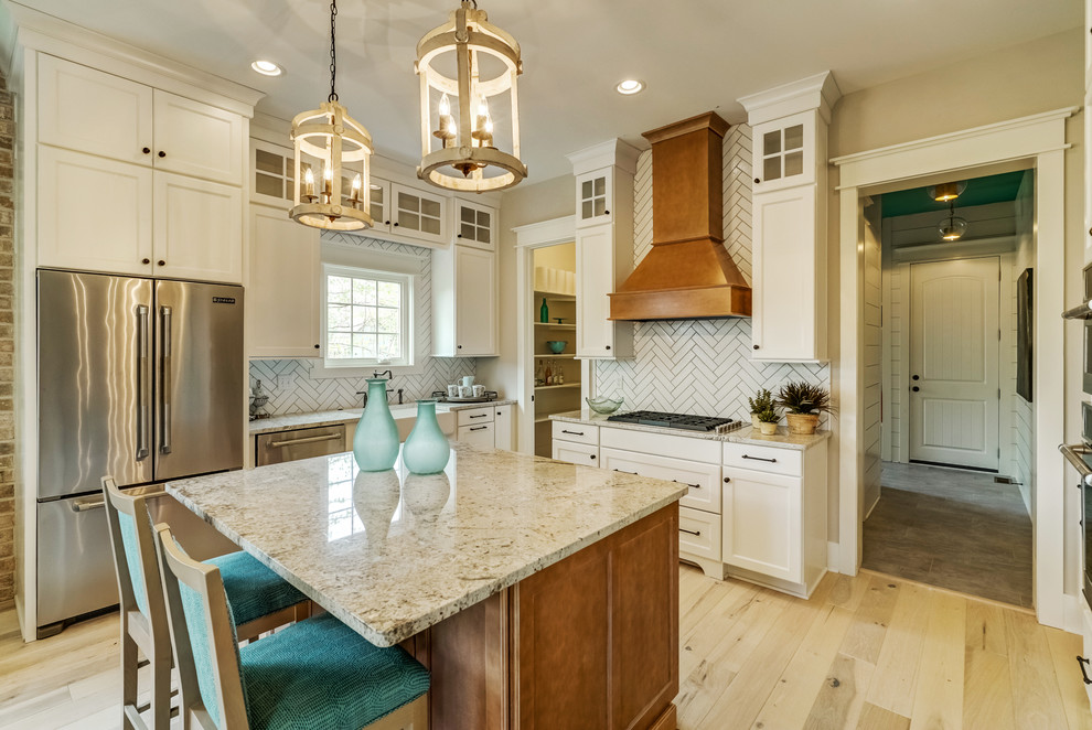 Foto de cocina tradicional cerrada con fregadero sobremueble, armarios estilo shaker, puertas de armario blancas, salpicadero blanco, electrodomésticos de acero inoxidable, suelo de madera clara, una isla, suelo beige y encimeras beige