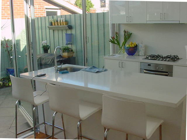 Idee per una piccola cucina abitabile design con ante lisce, ante bianche, top in superficie solida, paraspruzzi con lastra di vetro e parquet chiaro