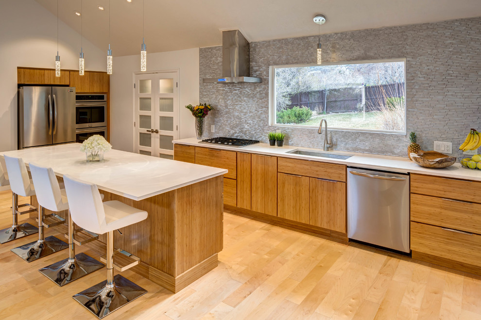 Medium sized modern galley kitchen/diner in Salt Lake City with a submerged sink, flat-panel cabinets, light wood cabinets, engineered stone countertops, grey splashback, glass tiled splashback, stainless steel appliances, light hardwood flooring and an island.