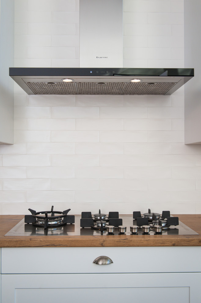 Foto på ett mellanstort nordiskt kök, med en dubbel diskho, skåp i shakerstil, vita skåp, bänkskiva i koppar, vitt stänkskydd, stänkskydd i tunnelbanekakel, rostfria vitvaror, betonggolv, en köksö och svart golv