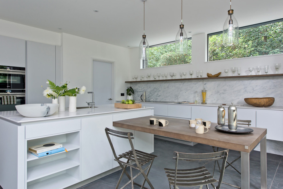 Eat-in kitchen - contemporary l-shaped porcelain tile and gray floor eat-in kitchen idea in London with flat-panel cabinets, white cabinets, marble countertops, gray backsplash, marble backsplash, stainless steel appliances, an island, an undermount sink and white countertops