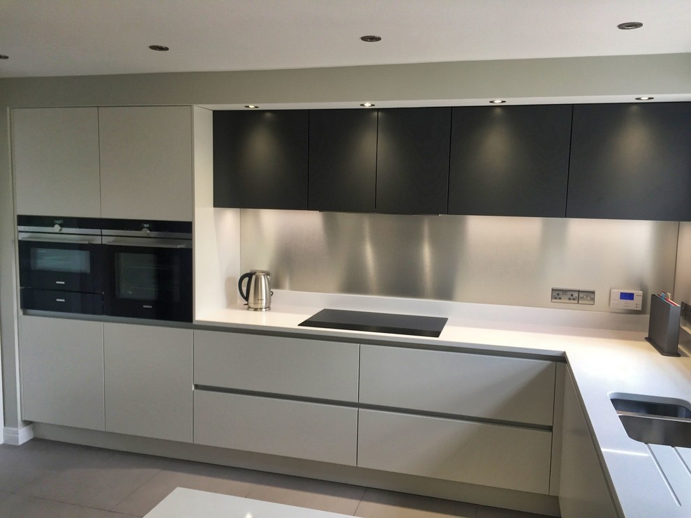 Photo of a medium sized contemporary u-shaped kitchen/diner in Cambridgeshire with a submerged sink, flat-panel cabinets, grey cabinets, quartz worktops, black appliances, ceramic flooring, a breakfast bar, grey floors and white worktops.