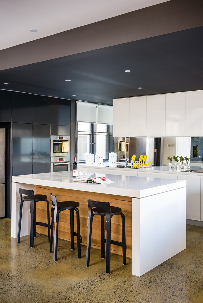 Bild på ett mellanstort funkis kök, med släta luckor, vita skåp, spegel som stänkskydd, rostfria vitvaror, betonggolv och en köksö
