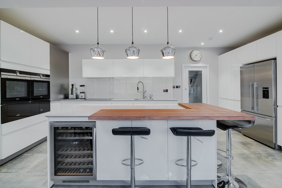Photo of a large modern l-shaped open plan kitchen in London with a submerged sink, flat-panel cabinets, white cabinets, composite countertops, white splashback, stainless steel appliances, porcelain flooring, an island and grey floors.
