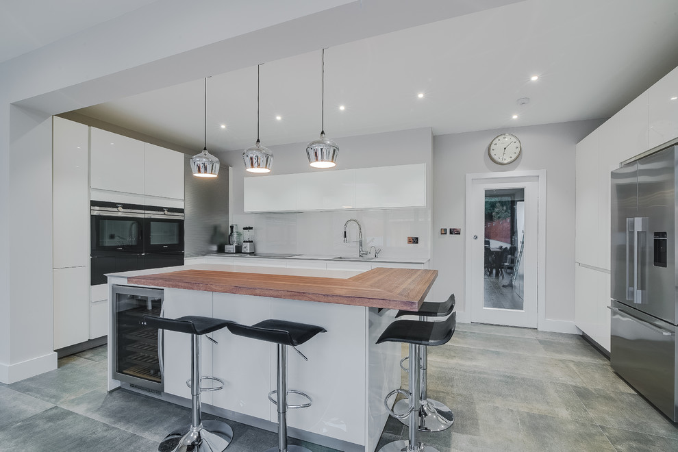 This is an example of a large contemporary l-shaped open plan kitchen in London with a submerged sink, flat-panel cabinets, white cabinets, composite countertops, white splashback, stainless steel appliances, porcelain flooring, an island and grey floors.