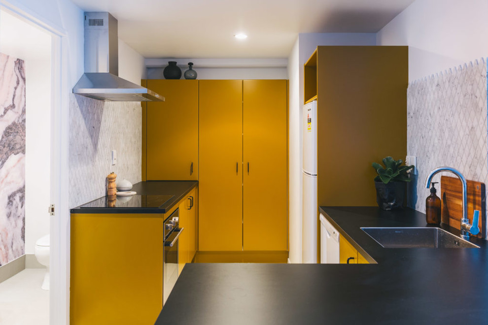 Offene, Kleine Shabby-Style Küche in U-Form mit Unterbauwaschbecken, flächenbündigen Schrankfronten, gelben Schränken, Rückwand aus Marmor, weißen Elektrogeräten und Halbinsel in Auckland
