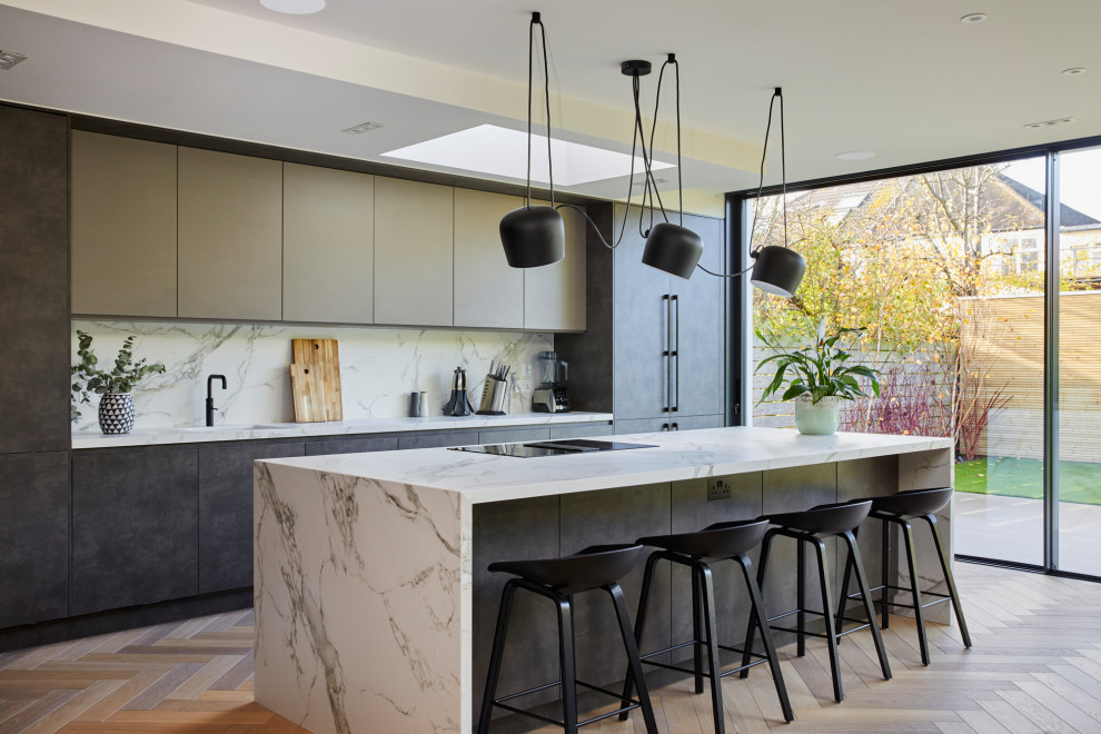 Contemporary galley kitchen in Surrey with a submerged sink, flat-panel cabinets, grey cabinets, white splashback, stone slab splashback, integrated appliances, light hardwood flooring, an island, beige floors and white worktops.