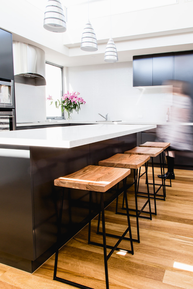 Offene, Mittelgroße Moderne Küche mit Doppelwaschbecken, Schrankfronten mit vertiefter Füllung, schwarzen Schränken, Granit-Arbeitsplatte, Küchenrückwand in Weiß, Küchengeräten aus Edelstahl, hellem Holzboden und Kücheninsel in Melbourne