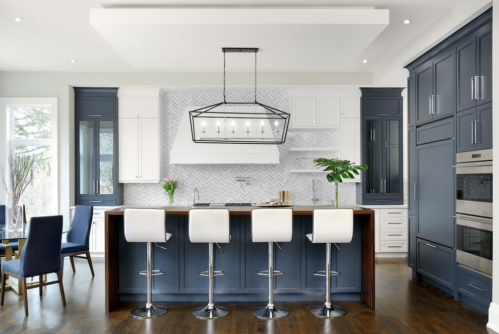 Example of a large transitional l-shaped dark wood floor and brown floor open concept kitchen design in Toronto with recessed-panel cabinets, blue cabinets, wood countertops, white backsplash, an island, a drop-in sink, marble backsplash and stainless steel appliances