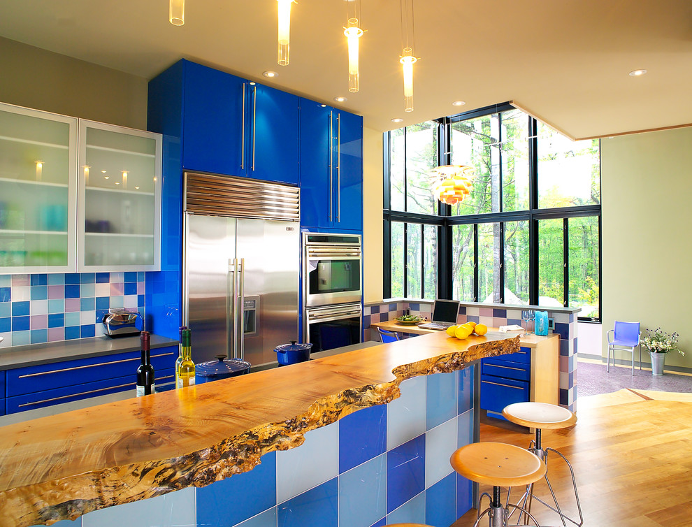 Cette photo montre une cuisine tendance avec un placard à porte plane, un plan de travail en bois, des portes de placard bleues, une crédence multicolore et un électroménager en acier inoxydable.