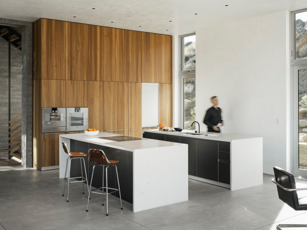 Idee per una cucina ad ambiente unico moderna con lavello sottopiano, ante lisce, ante in legno scuro, pavimento in cemento, 2 o più isole, pavimento grigio e top bianco