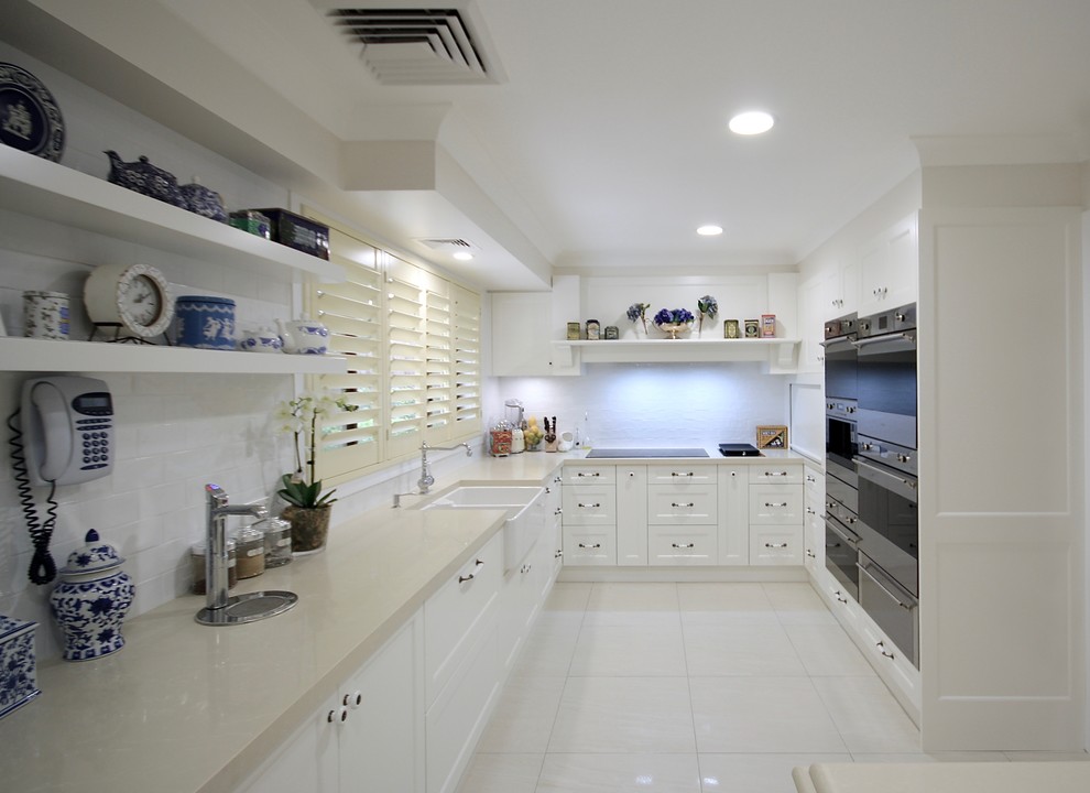 Example of a large classic u-shaped ceramic tile and beige floor open concept kitchen design in Sydney with a farmhouse sink, recessed-panel cabinets, white cabinets, quartz countertops, white backsplash, subway tile backsplash, stainless steel appliances, an island and beige countertops