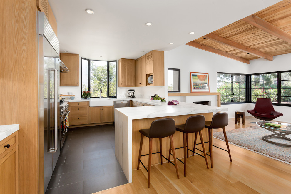 Mid-sized mid-century modern u-shaped light wood floor and yellow floor open concept kitchen photo in Los Angeles with a farmhouse sink, shaker cabinets, light wood cabinets, marble countertops, white backsplash, marble backsplash, stainless steel appliances and a peninsula