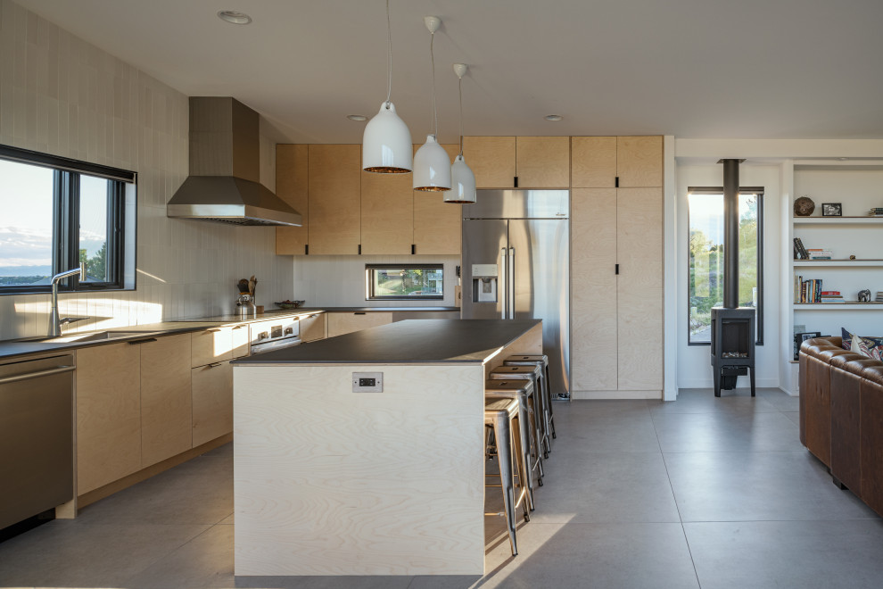 Medium sized modern l-shaped open plan kitchen in Boise with a submerged sink, flat-panel cabinets, light wood cabinets, white splashback, ceramic splashback, stainless steel appliances, concrete flooring, an island, grey floors, black worktops and a vaulted ceiling.