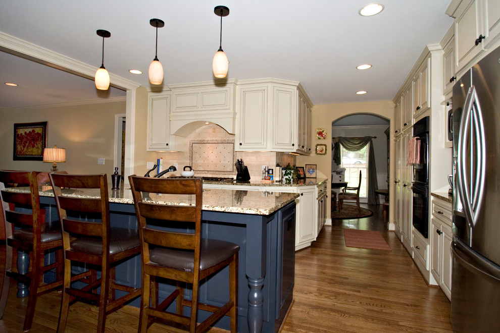Mid-sized arts and crafts l-shaped medium tone wood floor eat-in kitchen photo in Atlanta with an undermount sink, raised-panel cabinets, distressed cabinets, granite countertops, beige backsplash, subway tile backsplash, stainless steel appliances and an island