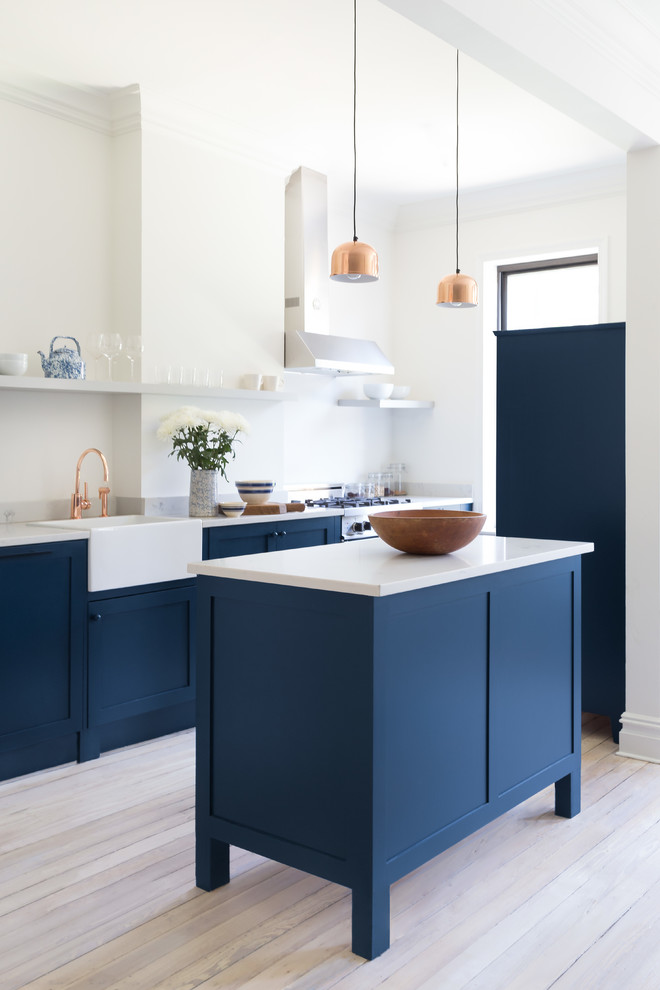 Diseño de cocina comedor actual con fregadero sobremueble, armarios estilo shaker, puertas de armario azules, encimera de cuarcita, electrodomésticos de acero inoxidable, suelo de madera clara, una isla y suelo blanco