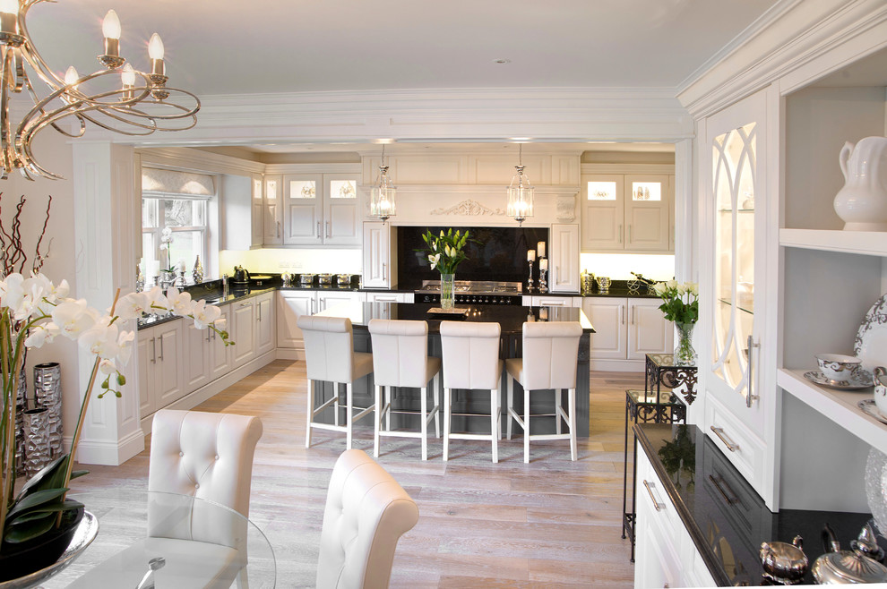 Inspiration for a large traditional u-shaped kitchen/diner in Other with an integrated sink, raised-panel cabinets, white cabinets, granite worktops, black splashback, stainless steel appliances, medium hardwood flooring, an island, brown floors and black worktops.