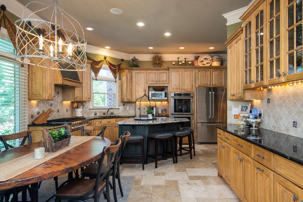 This is an example of a large classic l-shaped kitchen/diner in Atlanta with a built-in sink, glass-front cabinets, medium wood cabinets, laminate countertops, beige splashback, stone tiled splashback, stainless steel appliances, limestone flooring, an island, beige floors and black worktops.