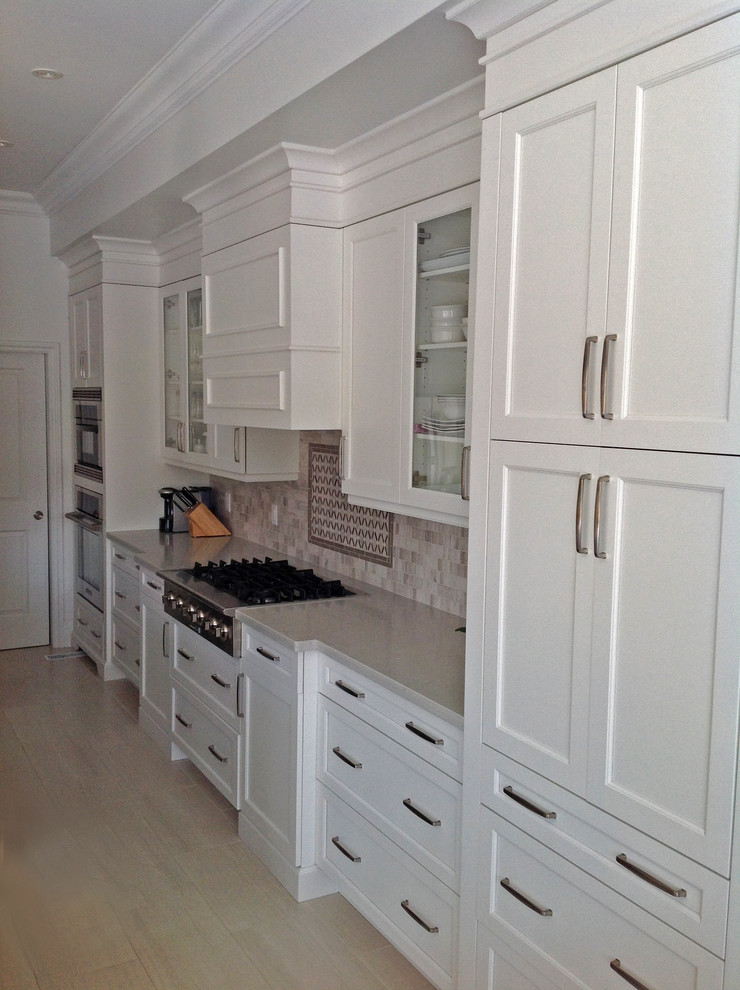 Example of a large transitional l-shaped porcelain tile eat-in kitchen design in Toronto with an undermount sink, recessed-panel cabinets, white cabinets, solid surface countertops, gray backsplash and stainless steel appliances