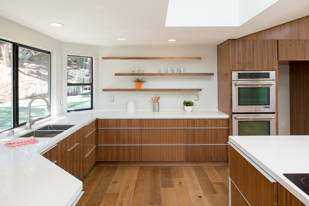 Example of a large minimalist u-shaped medium tone wood floor open concept kitchen design in San Diego with an undermount sink, flat-panel cabinets, dark wood cabinets, quartz countertops, white backsplash, stainless steel appliances and an island