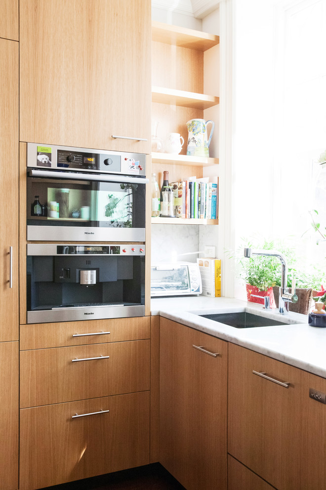 Modelo de cocina contemporánea con fregadero encastrado, armarios con paneles lisos, puertas de armario de madera clara, encimera de mármol y suelo de madera oscura