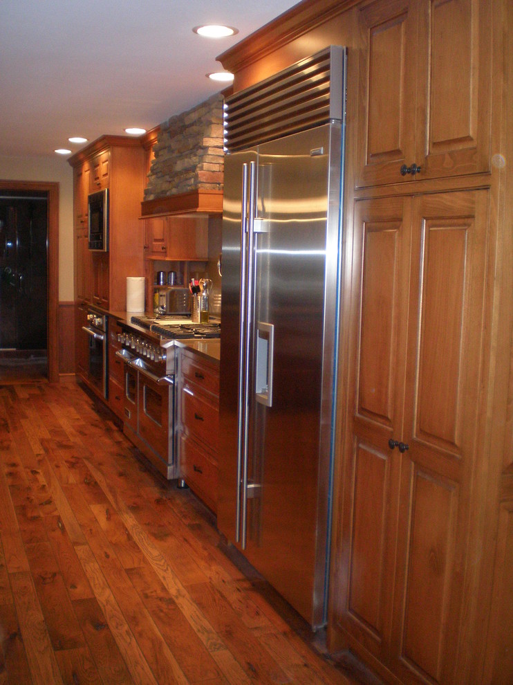 Idée de décoration pour une cuisine américaine linéaire tradition en bois brun avec un placard avec porte à panneau surélevé, un plan de travail en quartz modifié et un électroménager en acier inoxydable.