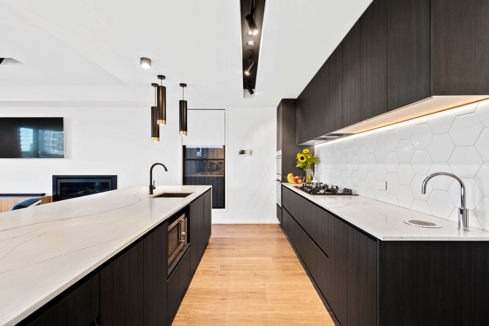 Ejemplo de cocina contemporánea con armarios con paneles lisos, suelo de madera en tonos medios, una isla, suelo marrón, encimeras blancas y con blanco y negro