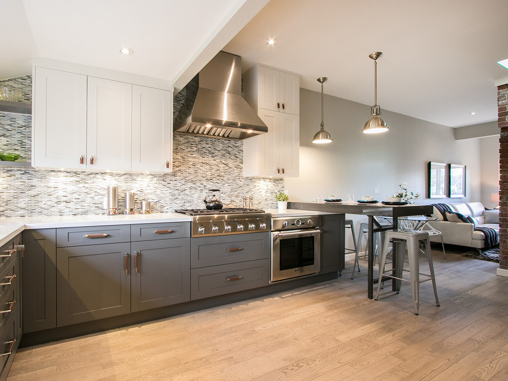 This is an example of a small eclectic u-shaped kitchen/diner in Vancouver with a submerged sink, shaker cabinets, grey cabinets, engineered stone countertops, blue splashback, glass tiled splashback, stainless steel appliances, light hardwood flooring and a breakfast bar.