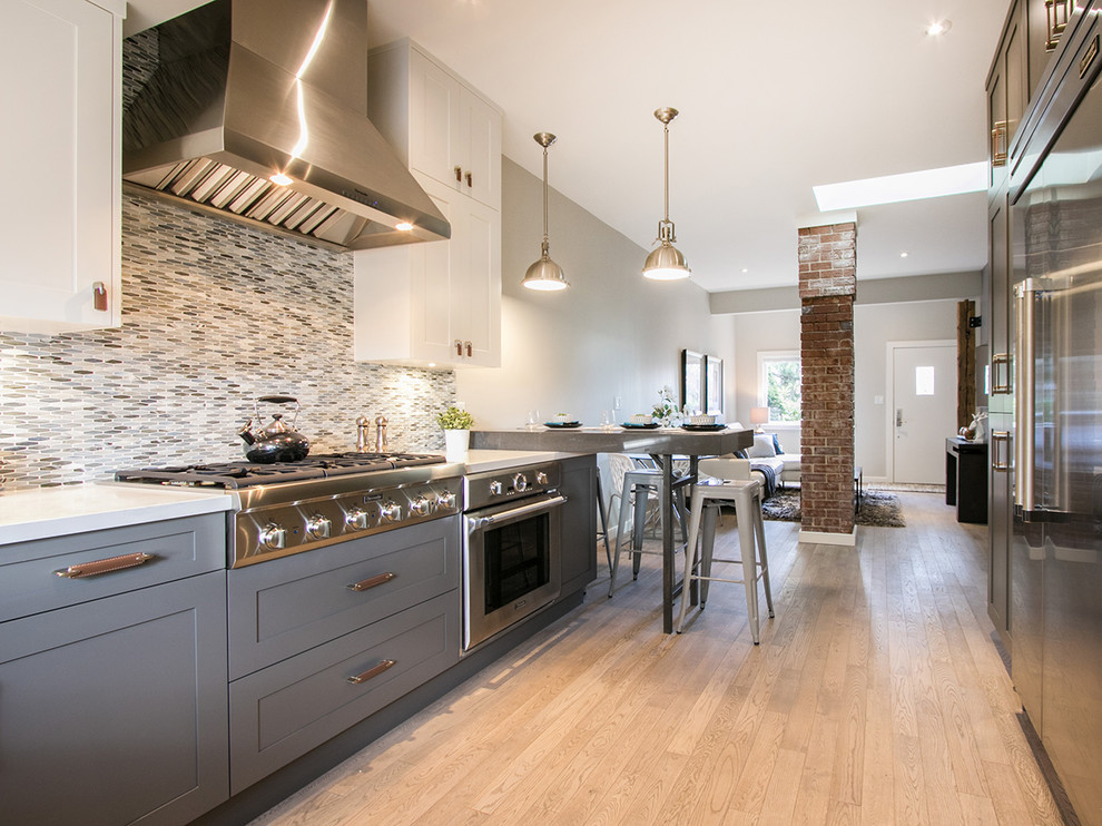 This is an example of a small classic u-shaped kitchen/diner in Vancouver with a submerged sink, shaker cabinets, grey cabinets, engineered stone countertops, blue splashback, glass tiled splashback, stainless steel appliances, light hardwood flooring and a breakfast bar.