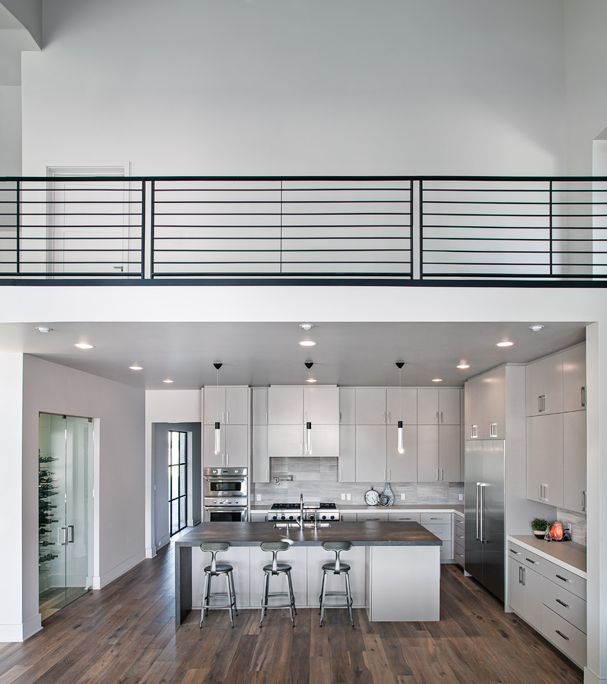 Inspiration for a mid-sized contemporary l-shaped dark wood floor and brown floor open concept kitchen remodel in Austin with an undermount sink, flat-panel cabinets, gray cabinets, solid surface countertops, white backsplash, stone tile backsplash, stainless steel appliances and an island