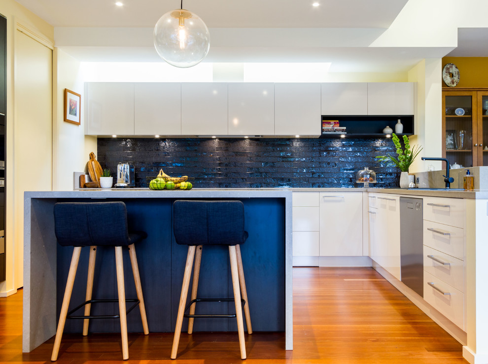 Example of a large trendy u-shaped medium tone wood floor open concept kitchen design in Melbourne with flat-panel cabinets, quartz countertops, black backsplash, subway tile backsplash, an island and gray countertops