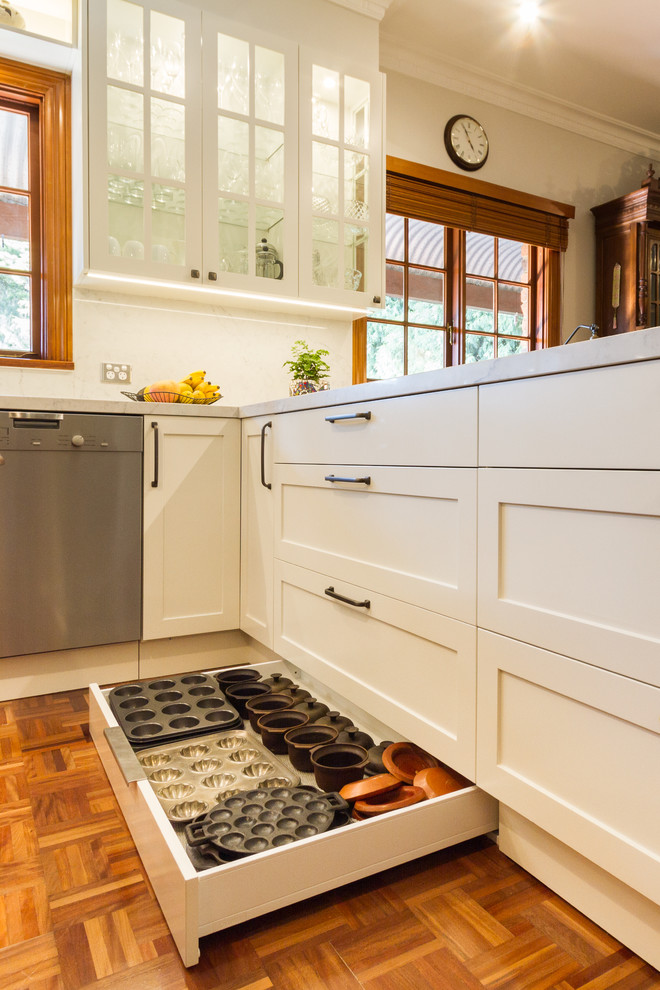 Example of a mid-sized classic u-shaped medium tone wood floor and brown floor eat-in kitchen design in Melbourne with a drop-in sink, shaker cabinets, white cabinets, marble countertops, white backsplash, marble backsplash, stainless steel appliances, a peninsula and white countertops