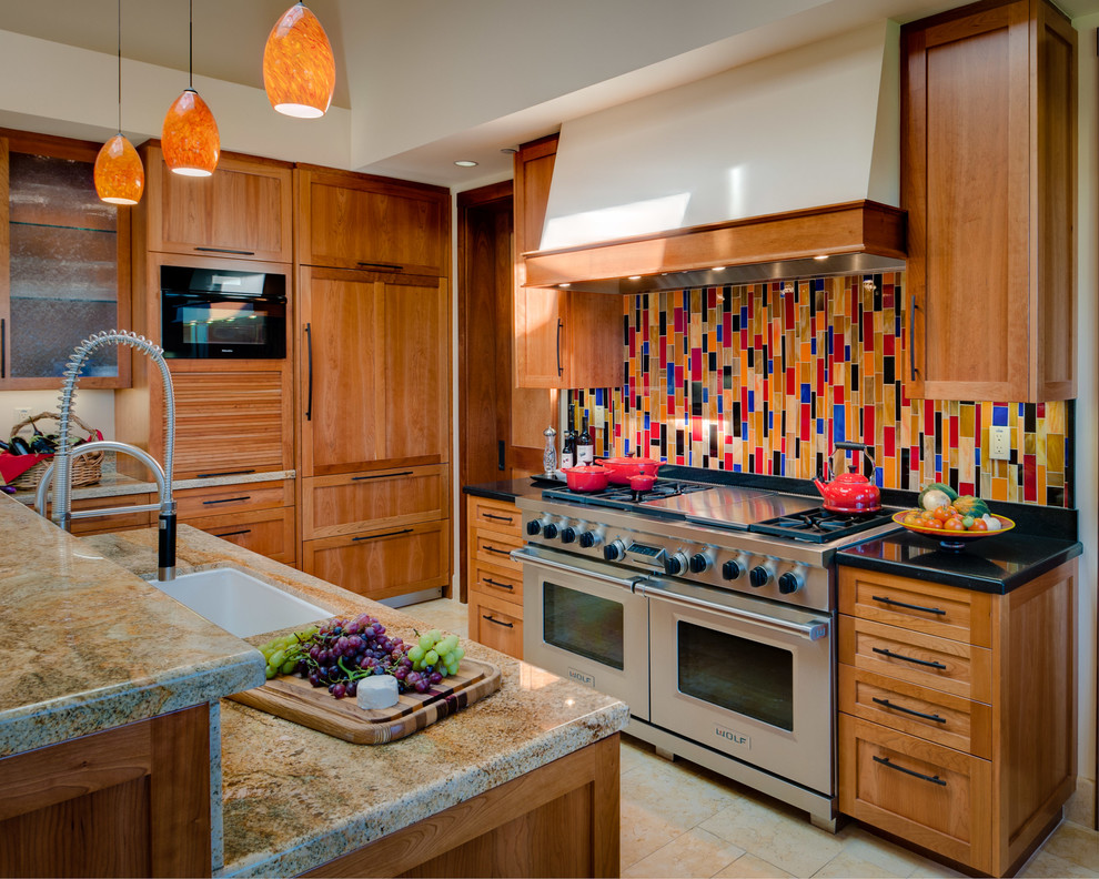 Amerikansk inredning av ett kök, med en undermonterad diskho, skåp i shakerstil, skåp i mellenmörkt trä, flerfärgad stänkskydd och en köksö