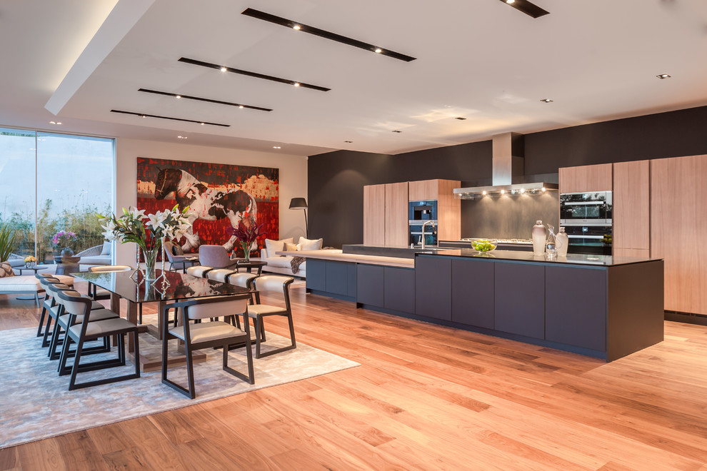 Offene, Zweizeilige Moderne Küche mit flächenbündigen Schrankfronten, hellen Holzschränken, Küchenrückwand in Grau, braunem Holzboden, Kücheninsel, braunem Boden und grauer Arbeitsplatte in Los Angeles