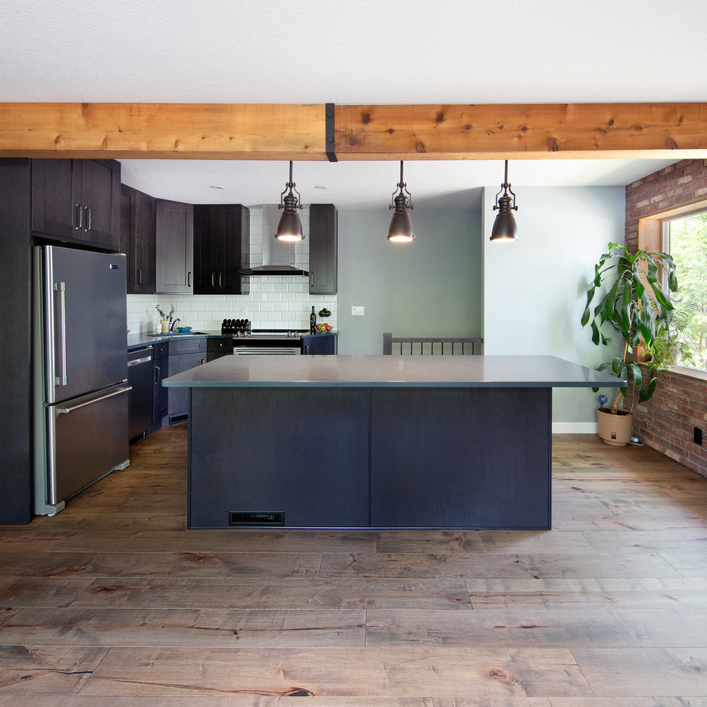 Inspiration for a small industrial l-shaped medium tone wood floor and brown floor open concept kitchen remodel in Edmonton with an undermount sink, recessed-panel cabinets, brown cabinets, quartzite countertops, white backsplash, ceramic backsplash, stainless steel appliances, an island and gray countertops