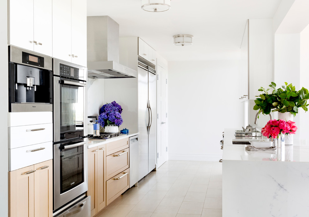This is an example of a large contemporary galley kitchen in New York with a submerged sink, shaker cabinets, light wood cabinets, marble worktops, white splashback, stone slab splashback, stainless steel appliances, porcelain flooring and a breakfast bar.