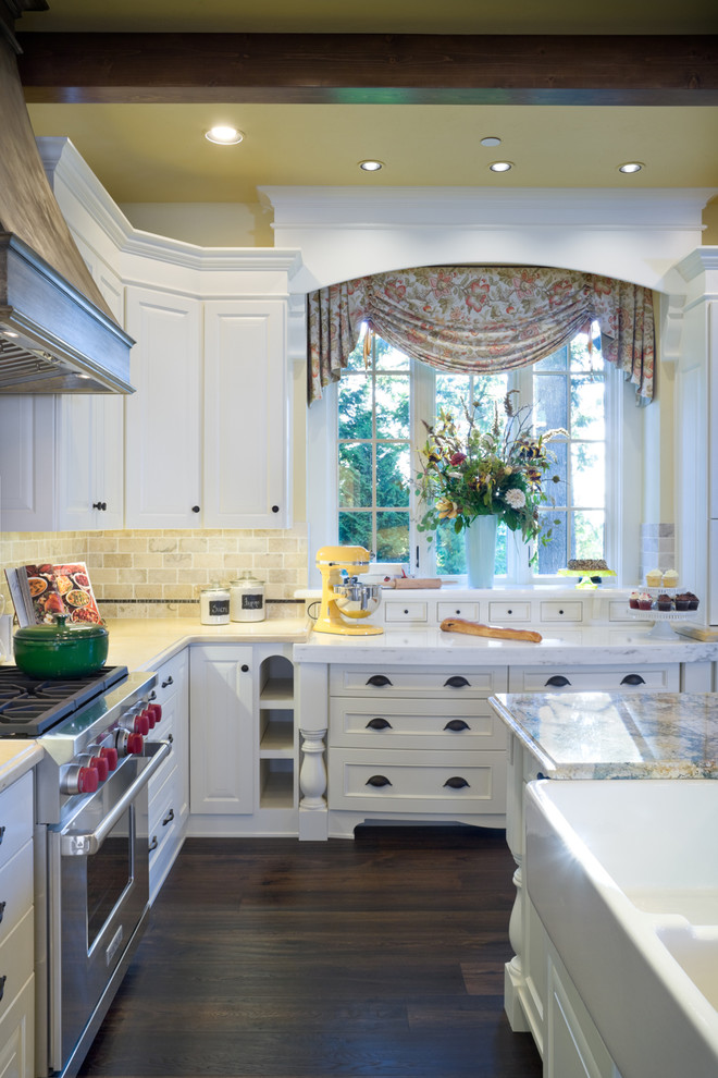 На фото: кухня в классическом стиле с белыми фасадами, бежевым фартуком, техникой из нержавеющей стали и окном с