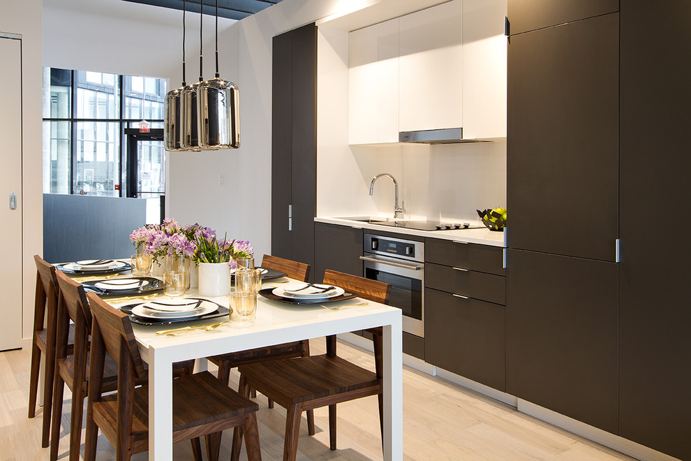 Imagen de cocina comedor lineal contemporánea pequeña con armarios con paneles lisos, puertas de armario grises, salpicadero blanco, electrodomésticos de acero inoxidable, suelo de madera clara, fregadero bajoencimera y encimeras blancas