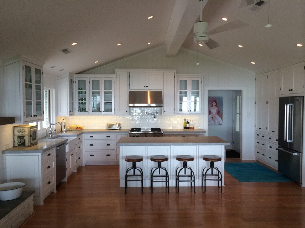 Example of a mid-sized classic l-shaped open concept kitchen design in Richmond with a farmhouse sink, glass-front cabinets, white cabinets, concrete countertops, white backsplash, porcelain backsplash, stainless steel appliances and an island