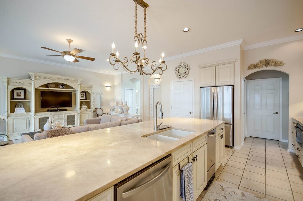 This is an example of a medium sized traditional galley open plan kitchen in Tampa with a submerged sink, raised-panel cabinets, beige cabinets, beige splashback, stainless steel appliances, an island, granite worktops, cement flooring, beige floors and beige worktops.