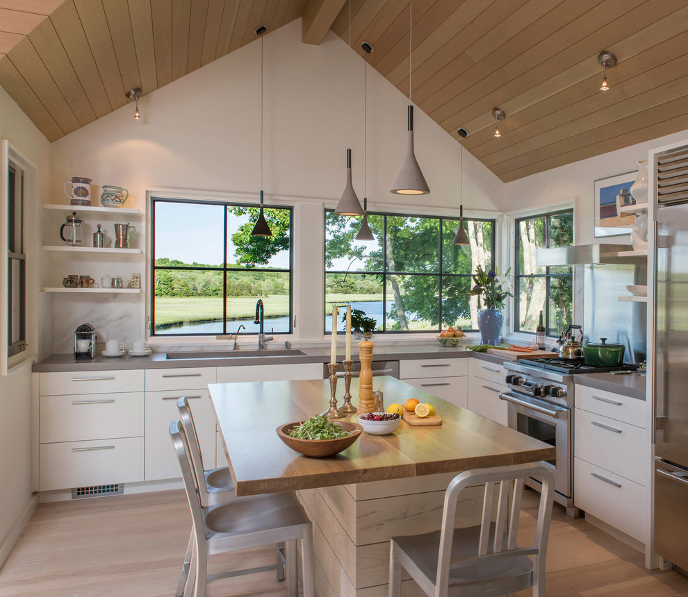 Immagine di una cucina stile marino con ante lisce, ante in legno chiaro, paraspruzzi a finestra, elettrodomestici in acciaio inossidabile e parquet chiaro