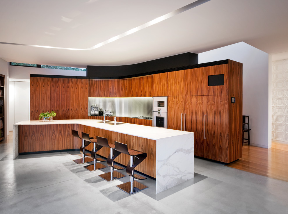 Bild på ett funkis kök, med skåp i mellenmörkt trä, stänkskydd med metallisk yta, betonggolv, en köksö, släta luckor, marmorbänkskiva och integrerade vitvaror