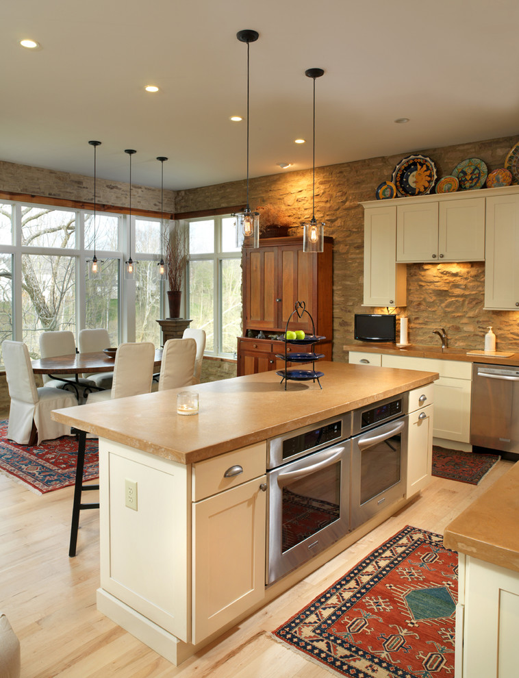 Rustik inredning av ett kök och matrum, med rostfria vitvaror, skåp i shakerstil, vita skåp, bänkskiva i betong och brunt stänkskydd