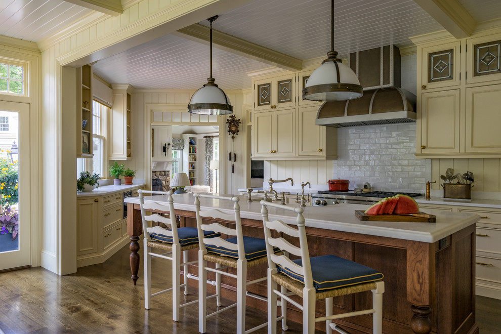 Bild på ett vintage vit vitt kök, med luckor med infälld panel, beige skåp, vitt stänkskydd, stänkskydd i tunnelbanekakel, rostfria vitvaror, mörkt trägolv och en köksö